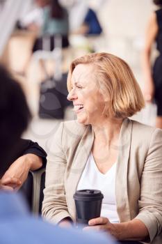 Mature Businesswoman Waiting In Airport Departure Lounge Drinking Coffee From Reusable Cup