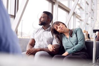 Tired Business Couple Sitting By Window Waiting In Airport Departure Lounge