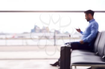 Defocused View Of Businessman Sitting In Airport Departure Lounge Using Mobile Phone