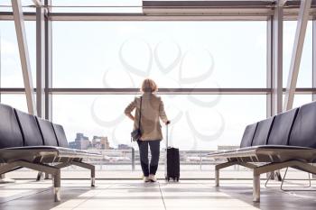 Rear View Of Businesswoman With Luggage Standing By Window In Airport Departure Lounge