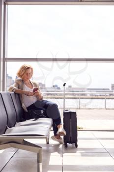 Mature Businesswoman Sitting In Airport Departure Lounge Using Mobile Phone