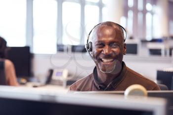 Portrait Of Mature Businessman Wearing Telephone Headset Working In Customer Services Department
