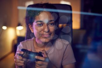 Teenage Girl With Game Pad Sitting In Chair and Gaming At Home With Screen Reflection