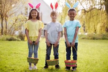 Portrait Of Three Children Wearing Bunny Ears On Easter Egg Hunt In Garden