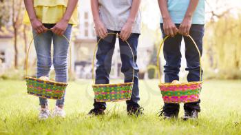 Close Up Of Three Children Holding Baskets On Easter Egg Hunt In Garden