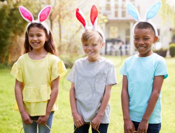Portrait Of Three Children Wearing Bunny Ears On Easter Egg Hunt In Garden
