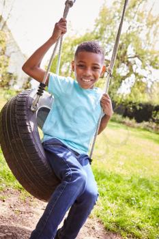 Portrait Of Smiling Boy Having Fun Playing On Tire Swing In Garden