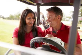 Mature Couple Playing Golf Marking Scorecard In Buggy Driving Along Course