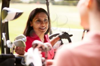 Two Women Playing Golf Driving Buggy And Talking Over Clubs