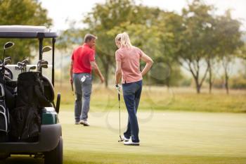 Rear View Of Couple Getting Out Of Golf Buggy To Play Shot On Green