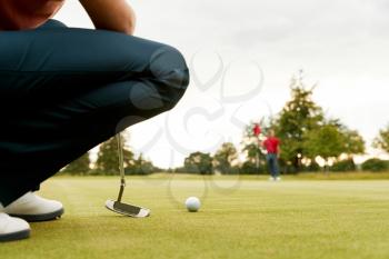 Close Up Of Female Golfer Lining Up Shot On Putting Green As Man Tends Flag