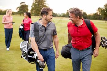 Two Mature Couples Playing Round Of Golf Carrying Golf Bags Along Fairway