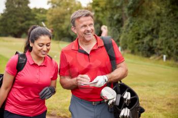 Mature Couple Playing Round Of Golf Carrying Golf Bags And Marking Scorecard