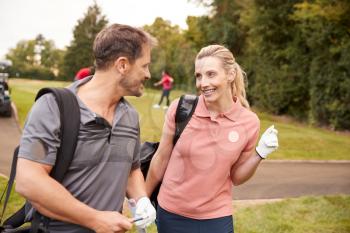 Mature Couple Playing Round Of Golf Carrying Golf Bags And Talking