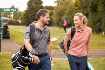 Mature Couple Playing Round Of Golf Carrying Golf Bags And Talking