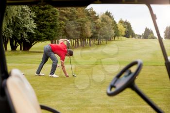 Mature Male Golfer Preparing To Hit Tee Shot Along Fairway With Driver Viewed Through Buggy Window