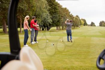 Two Couples Golfing Hitting Tee Shot Along Fairway With Driver With Buggy In Foreground