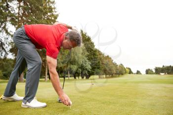 Mature Male Golfer Preparing To Hit Tee Shot Along Fairway With Driver