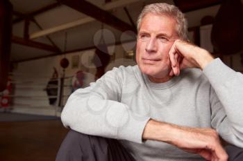 Portrait Of Senior Male Boxing Coach In Gym Standing By Old Fashioned Leather Punching Bags