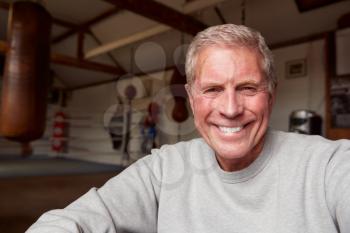 Portrait Of Smiling Senior Male Boxing Coach In Gym Standing By Old Fashioned Leather Punching Bags