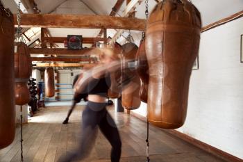Action Shot Of Male And Female Boxers In Gym Training With Leather Punch Bags