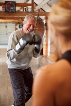 Senior Male Boxer Sparring With Younger Female Coach In Gym Using Training Gloves