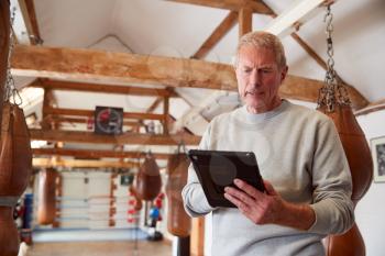 Senior Male Boxing Coach In Gym Tracking Training Using Digital Tablet