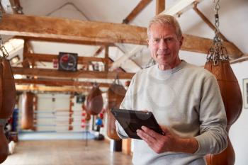 Portrait Of Senior Male Boxing Coach In Gym Tracking Training Using Digital Tablet