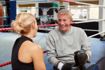 Personal Trainer Helping Senior Male Boxer In Gym To Put On Boxing Gloves In Gym