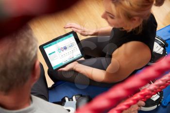 Female Personal Trainer With Senior Male Boxer In Gym Checking Performance Using Digital Tablet