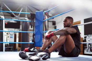 Tired Male Boxer Sitting In Boxing Ring In Gym After Training Session