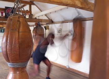 Action Shot Of Male Boxer In Gym Training With Leather Punch Bags