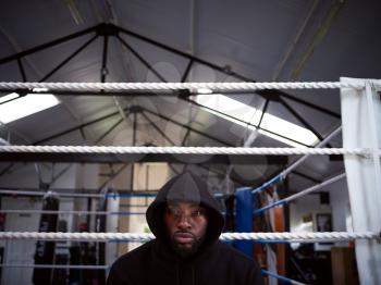 Portrait Of Male Boxer Training In Gym Wearing Hooded Sweatshirt Sitting By Boxing Ring