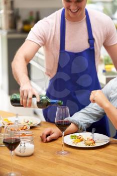 Man Pouring Wine For Group Of Friends Sitting Around Table Eating Meal At Home Together