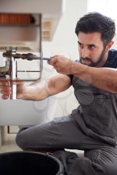Male Plumber Using Wrench To Fix Leaking Sink In Home Bathroom