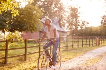 Young Woman Riding Bike Along Country Lane At Sunset