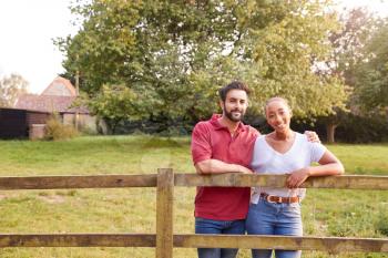 Portrait Of Romantic Couple Taking A Break And Resting On Fence During Walk In Countryside