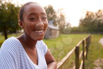 Portrait Of Smiling Young Woman Taking A Break And Resting On Fence During Walk In Countryside