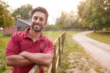 Portrait Of Smiling Man Taking A Break And Resting On Fence During Walk In Countryside