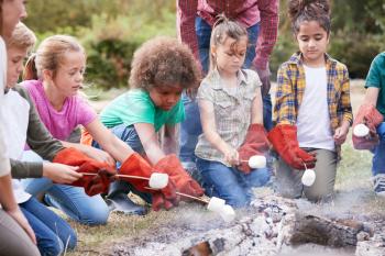 Team Leader With Group Of Children On Outdoor Activity Trip Toasting Marshmallows Over Camp Fire