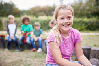 Portrait Of Girl On Outdoor Activity Camping Trip Sitting Around Camp Fire With Friends