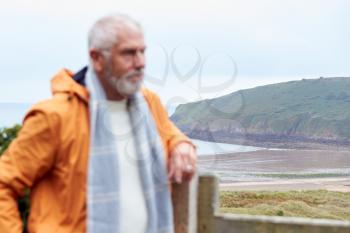 Defocused Shot Of Active Senior Man Walking Along Coastal Path In Fall Or Winter By Gate