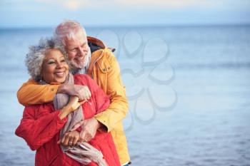 Loving Senior Couple Hugging As They Walk Along Shoreline On Winter Beach Vacation