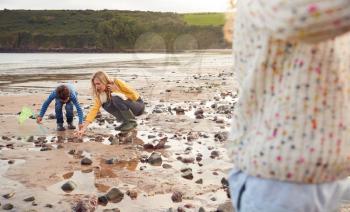 Family Looking In Rockpools On Winter Beach Vacation