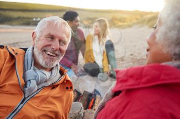 Loving Senior Couple Relaxing By Fire With Adult Offspring On Winter Beach Vacation