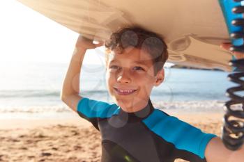 Portrait Of Smiling Boy Wearing Wetsuit Carrying Bodyboards On  Summer Beach Vacation