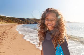 Portrait Of Young Girl Wearing Wetsuit Standing By Waves On Summer Beach Vacation