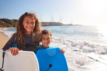 Portrait Of Children Wearing Wetsuits Holding Bodyboards On Summer Beach Vacation Having Fun By Sea