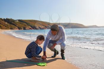 Father And Son Walking Along Beach By Breaking Waves On Beach With Fishing Net Finding Seaweed