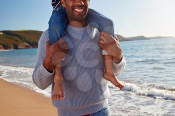 Close Up Of Loving Father Giving Son Ride On Shoulders As They Walk Along Beach Together